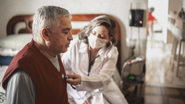 Health visitor listening to heartbeat of senior man during home visit